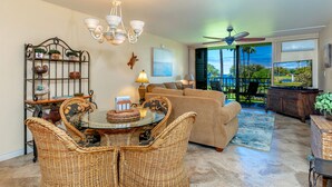 A spacious living room with a glass dining table, wicker chairs, a beige sofa, and a ceiling fan.