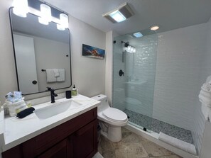 A modern bathroom with a large mirror, white sink, dark vanity, toilet, and a glass-enclosed shower.