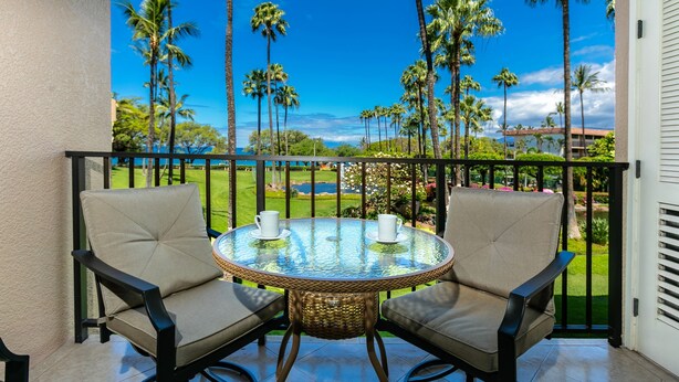 A balcony with two chairs and a table, overlooking a scenic view of palm trees and a golf course.