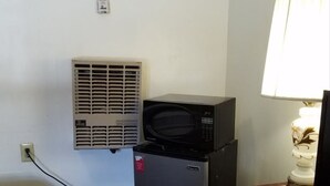 Une pièce compacte avec une kitchenette comprenant un réfrigérateur, un four à micro-ondes et un extracteur d’air. On y trouve une lampe sur une table en bois et un couvre-lit à motifs.
