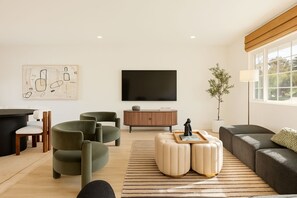 Una sala de estar moderna con un televisor de pantalla plana, sillones verdes, un sofá y una mesita de noche con una escultura.