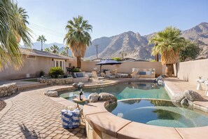 A pool area with lounge chairs, a table with a bottle and glasses, and a view of mountains in the background.