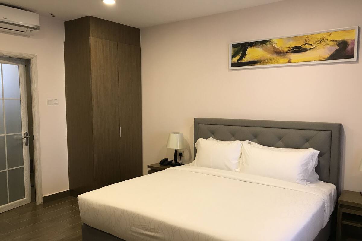 A hotel room with a large bed, a nightstand with a lamp, a painting on the wall, and a wardrobe.
