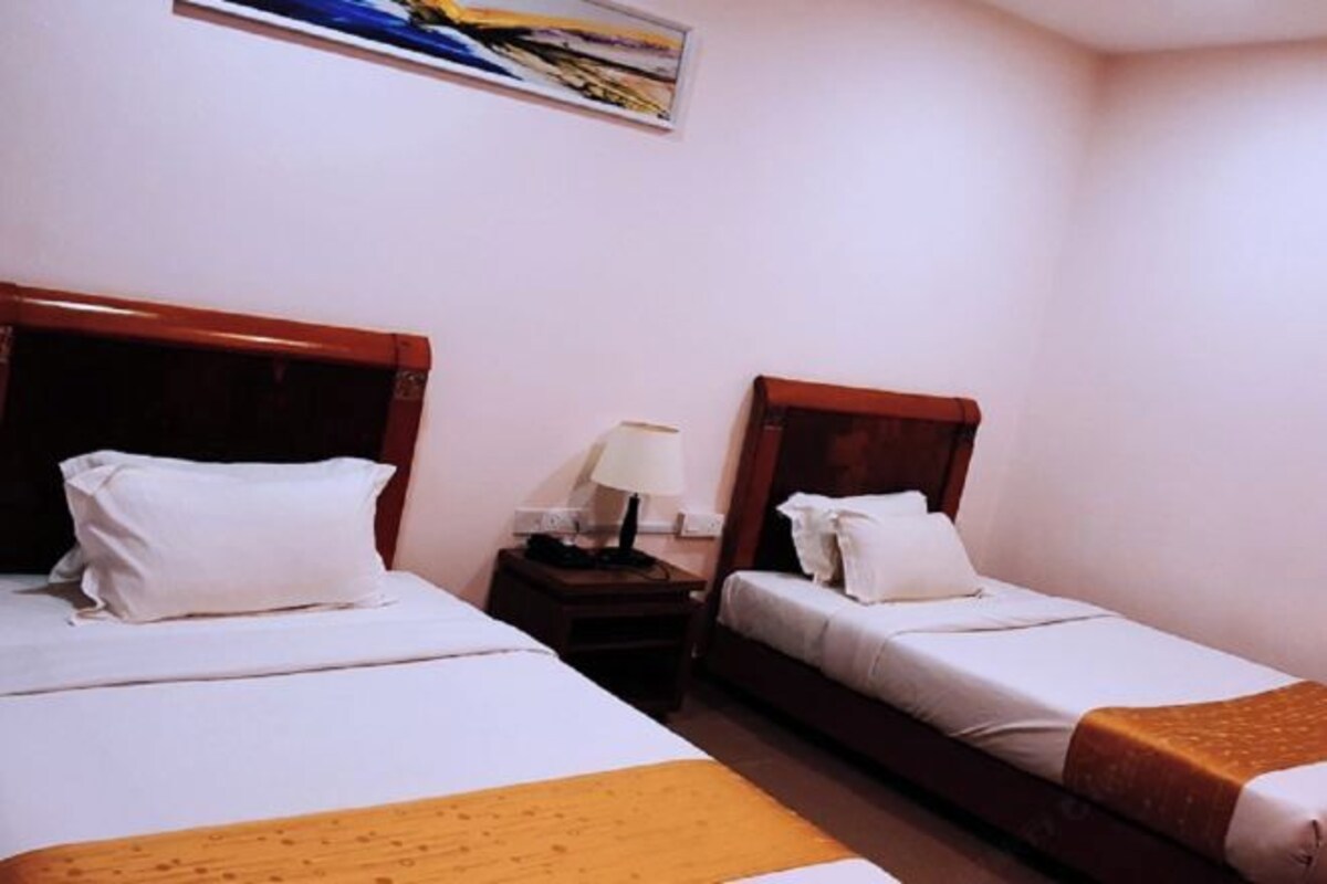 Una habitación de hotel con dos camas individuales, una mesita de noche con lámpara y un cuadro en la pared.