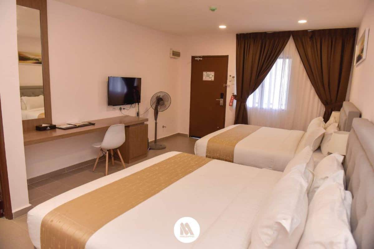 A hotel room with two beds, a desk with a chair, a television, and a fan.