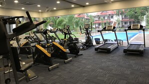 A gym with various exercise equipment, a pool, and a view of a residential area. - Lotus Seaview Beach Resort (Bandar Penawar)