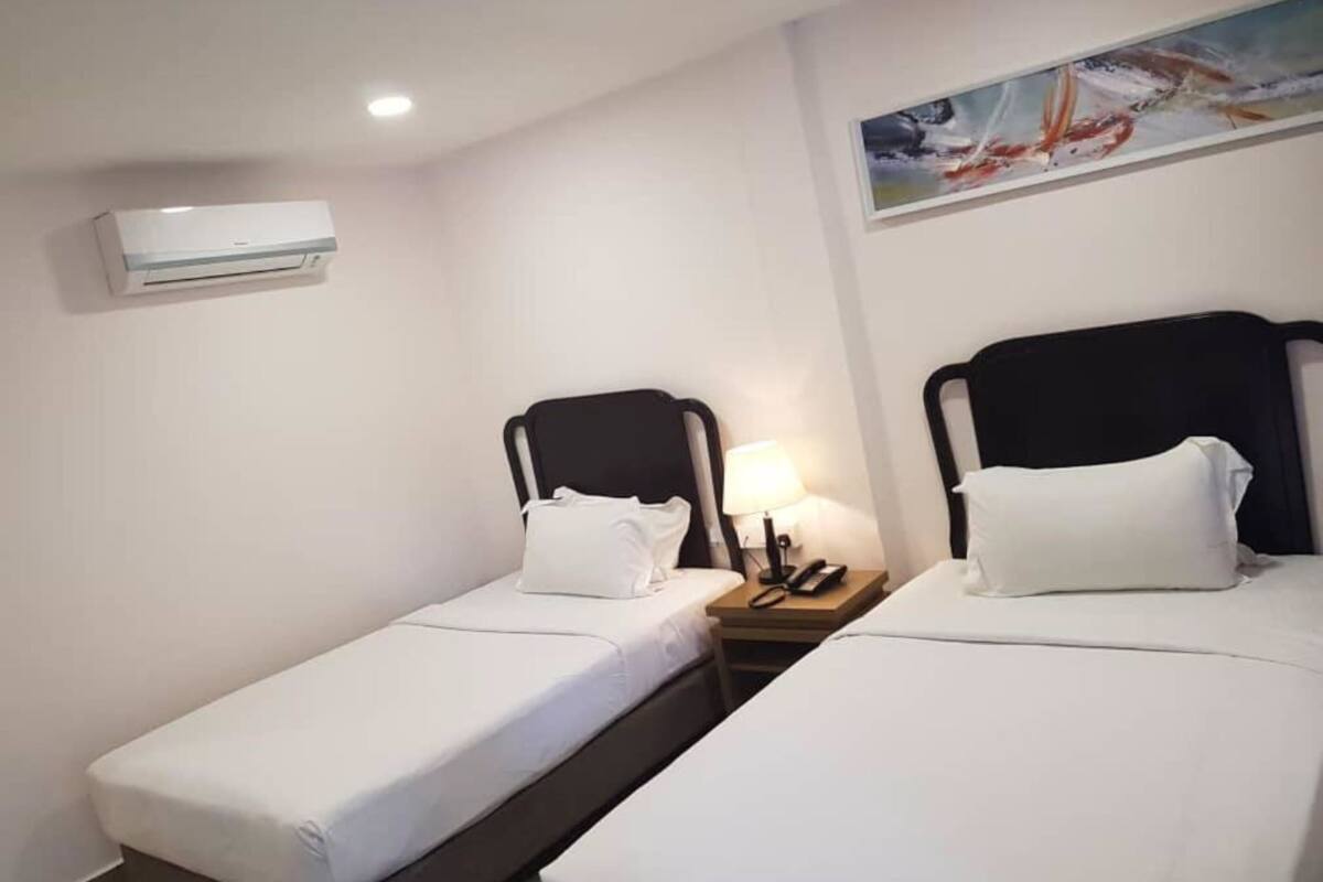 A hotel room with two single beds, a nightstand with a lamp, and a painting on the wall.