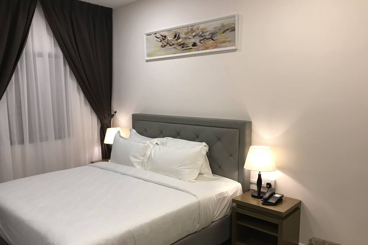 A neatly made bed with white linens, a grey upholstered headboard, and two bedside lamps.