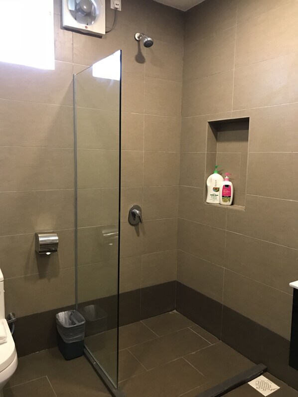 A modern bathroom with a glass shower enclosure, a toilet, a trash bin, and a shelf with toiletries.
