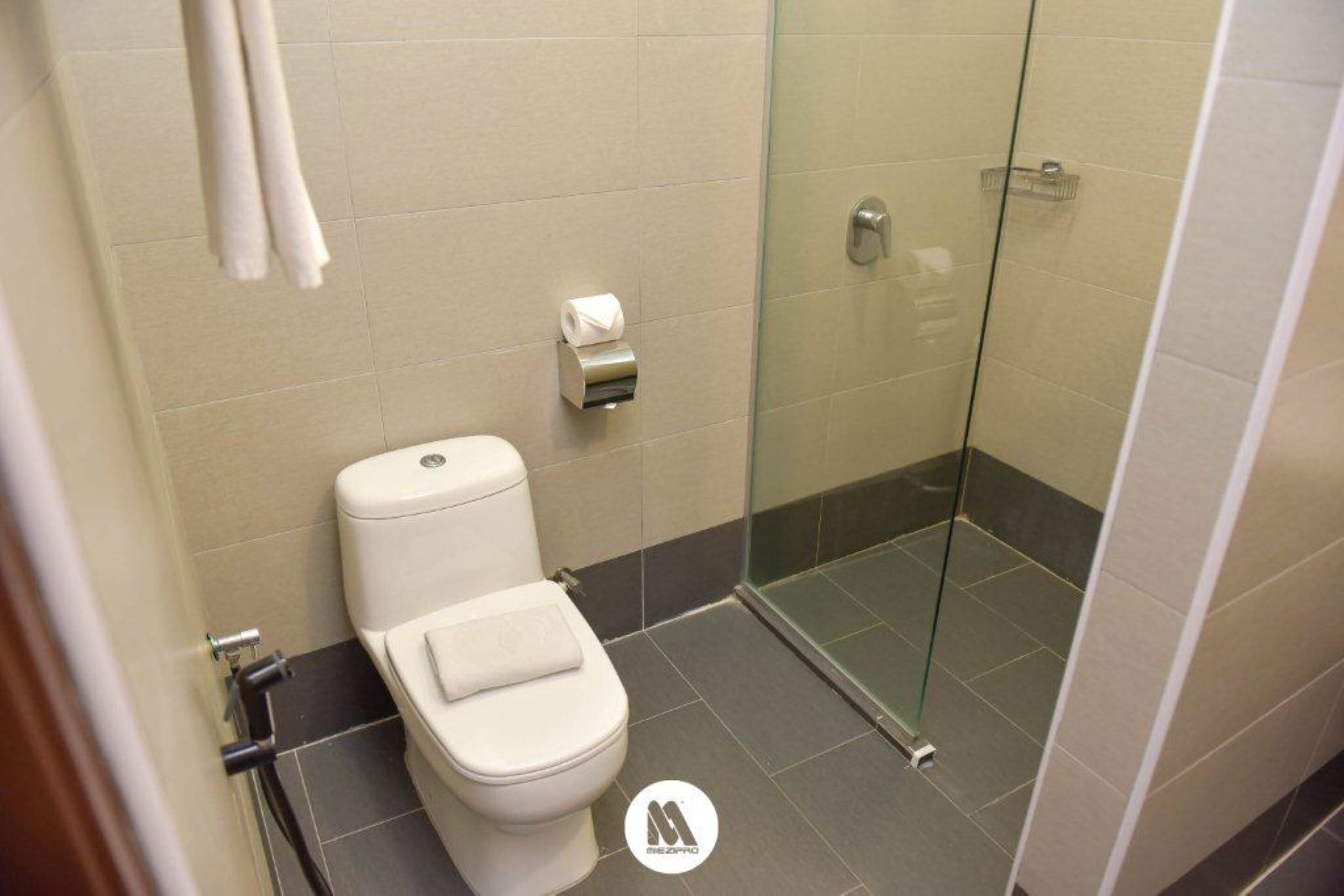 Un baño moderno con inodoro, cabina de ducha de vidrio y dispensador de toallas.