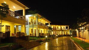 A multi-story hotel with balconies, a wet ground, and well-lit windows.
