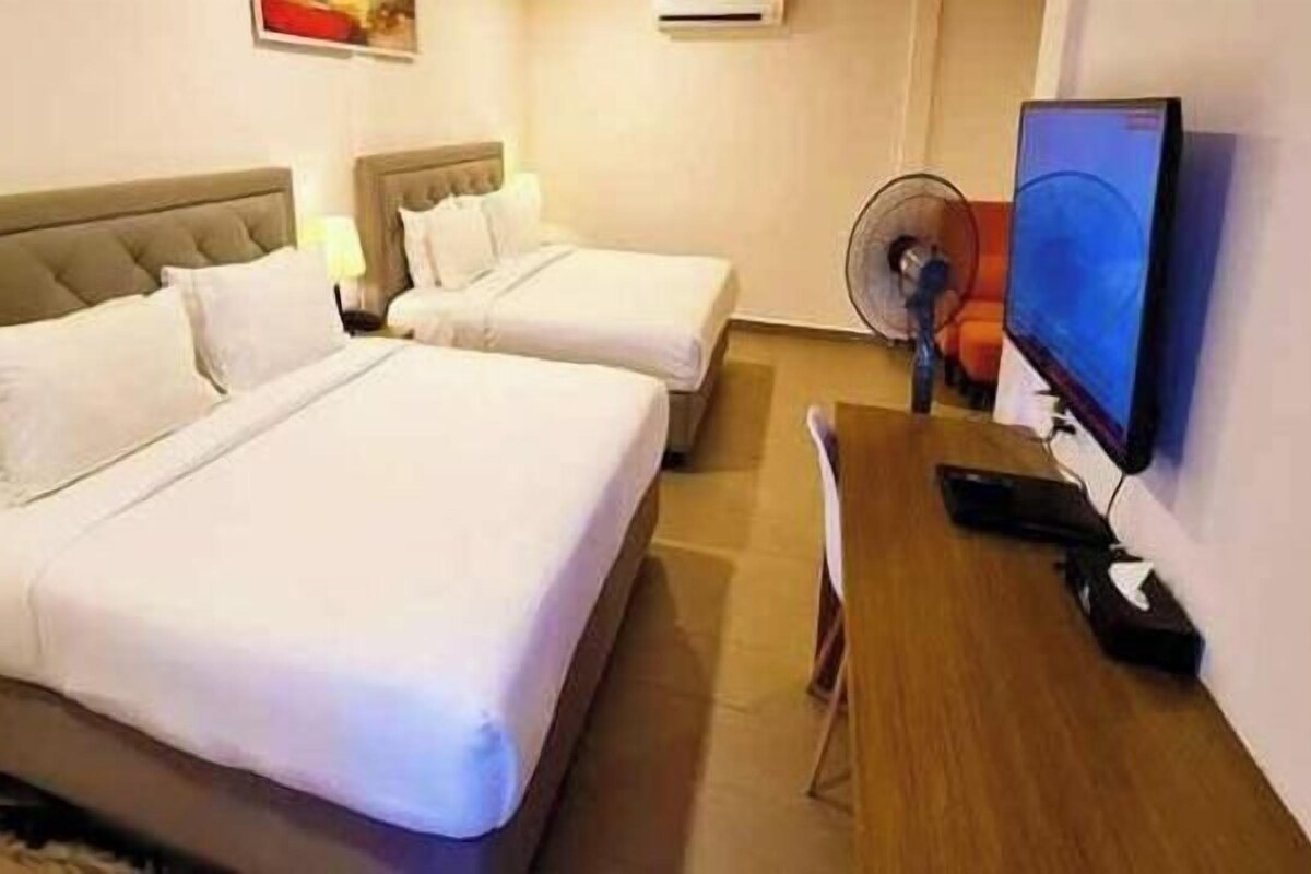 Habitación de hotel con dos camas, un escritorio con computadora y una televisión.