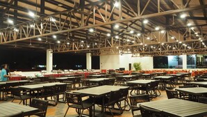 A spacious outdoor dining area with multiple tables and chairs, a high ceiling with exposed beams, and a view of the night sky. - Lotus Seaview Beach Resort (Bandar Penawar)