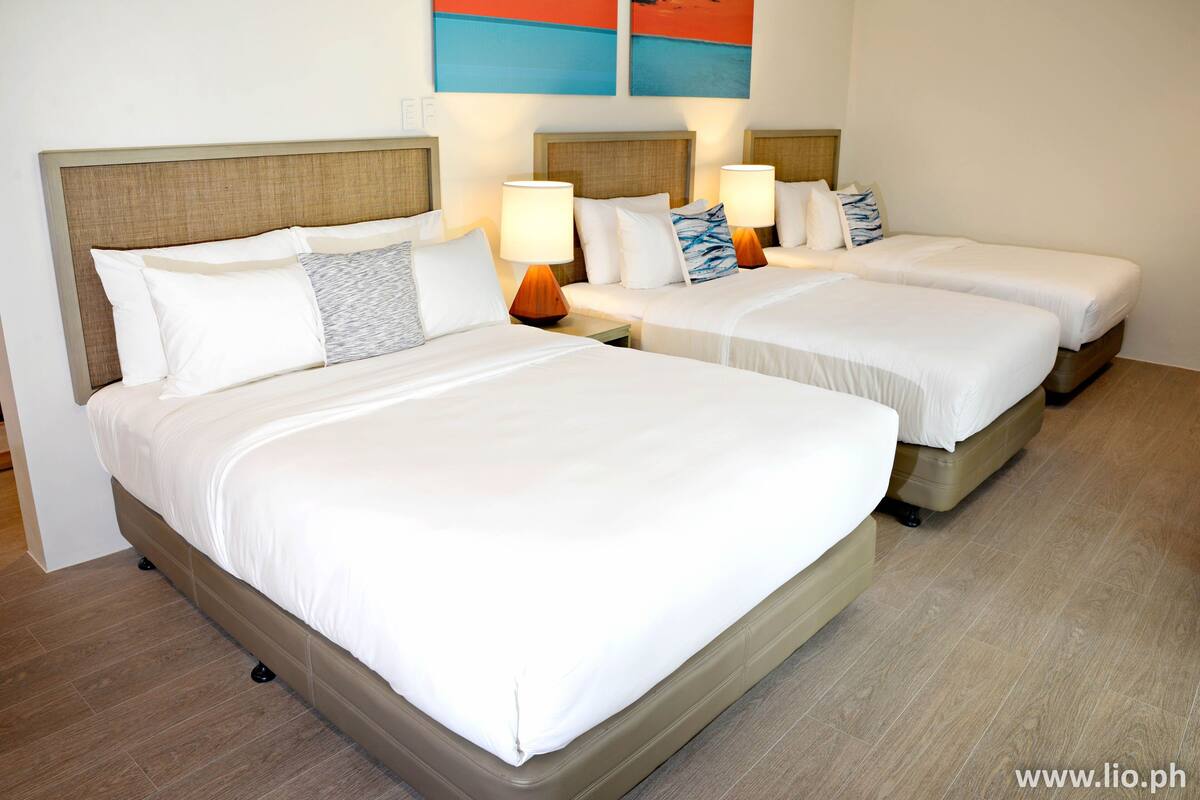 Ein Hotelzimmer mit zwei Betten, jeweils mit weißer Bettwäsche und hölzernen Kopfteilen. An den Nachttischen stehen Lampen und Zierkissen.