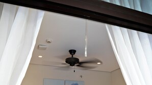 Une chambre d’hôtel comprenant un lit, deux tables de chevet, un ventilateur de plafond et deux lampes fixées au mur.