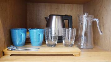 A wooden shelf with a stainless steel kettle, a glass carafe, and three blue mugs.