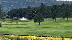 Un campo de golf con una fuente, árboles y una colina al fondo.