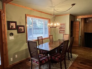 A dining area with a wooden table and chairs, a chandelier, a window with blinds, and a sign on the wall. - Mountain Retreat: 5 min walk to lake & hiking and 4 min drive to golf & slopes.  (Angel Fire)