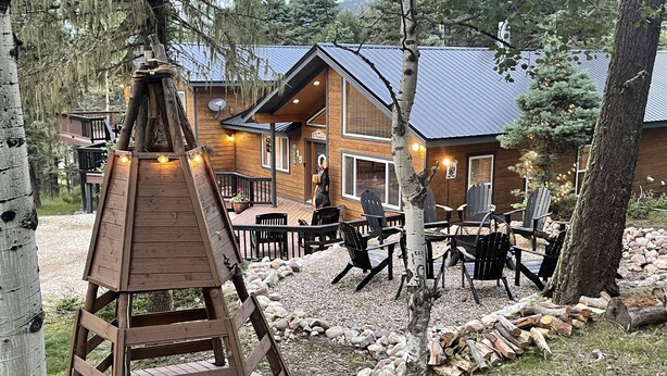 Una cabaña de madera con terraza, mobiliario exterior y vistas del bosque circundante.