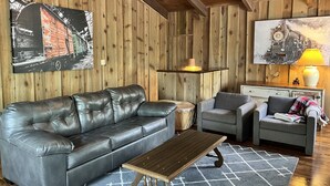 Una sala de estar acogedora con un sofá de cuero, una mesa de centro de madera y dos sillones.