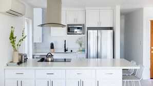 A modern kitchen with white cabinetry, a stainless steel refrigerator, a microwave, and a large island with bar stools. - Avalon 2 Unit Buyout (I & III) AvantStay | Mins to Gaslamp| Beautiful Deck w/BBQ (San Diego)