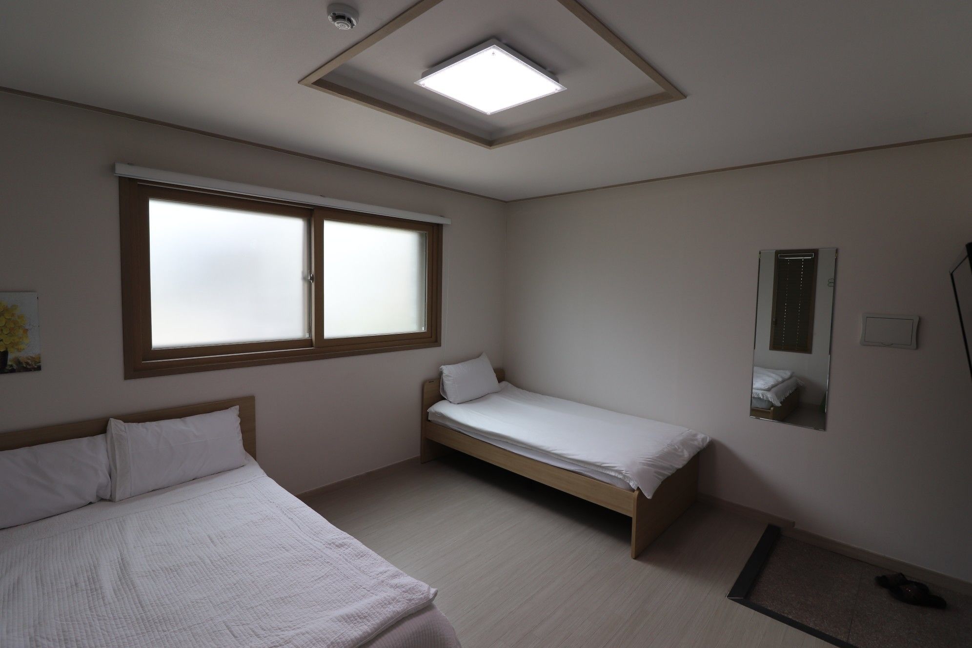 Een slaapkamer met twee enkele bedden, een dakraam, een raam en een spiegel.