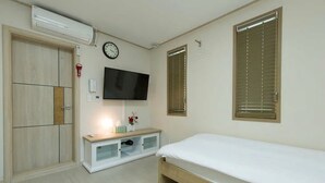 A bedroom with a bed, a TV mounted on the wall, a wardrobe, and a window with blinds. - Hub Guest House (Incheon)