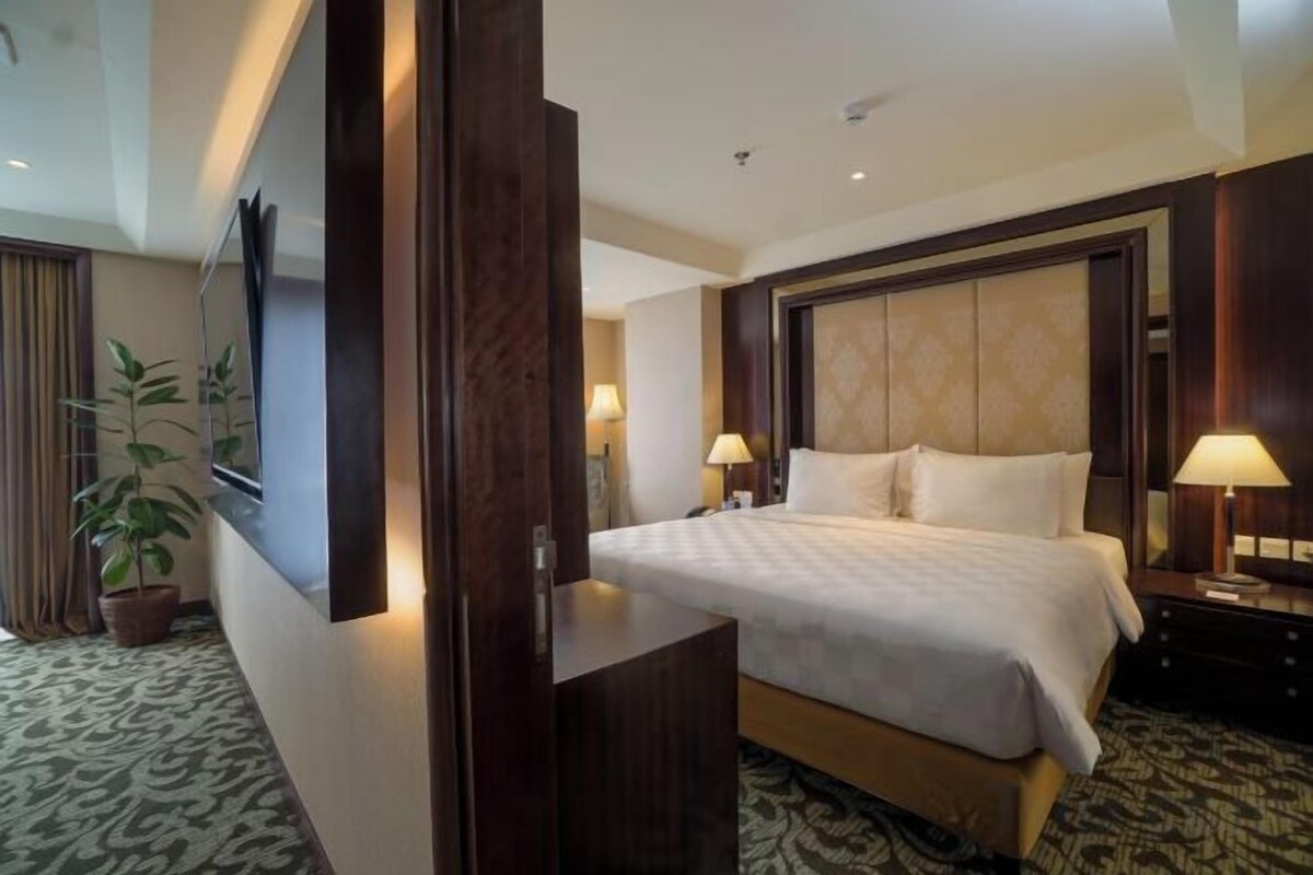 Ein Hotelzimmer mit einem großen Bett, Nachttischlampen, einem Flachbildfernseher, einem Holz-Kopfteil und einer Topfpflanze.