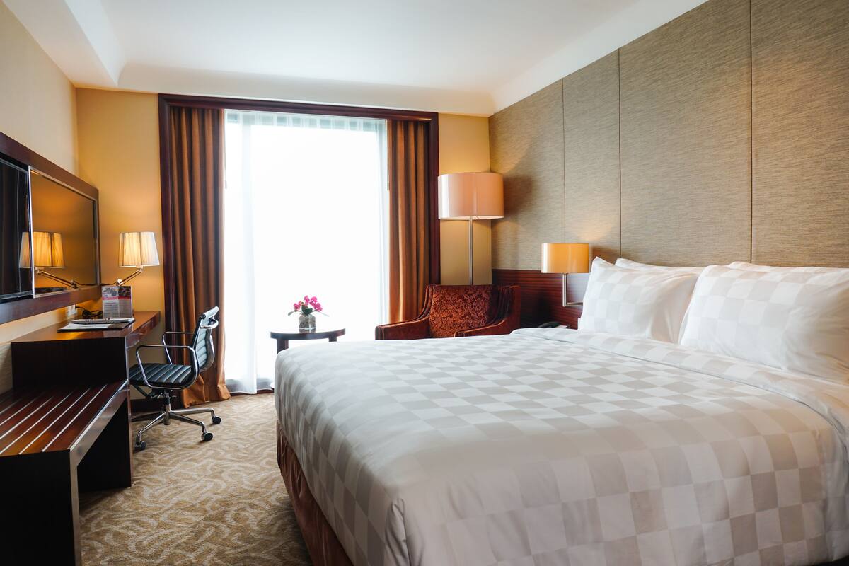 Une chambre d’hôtel avec un grand lit, un bureau avec une chaise, une tél évision et une lampe.