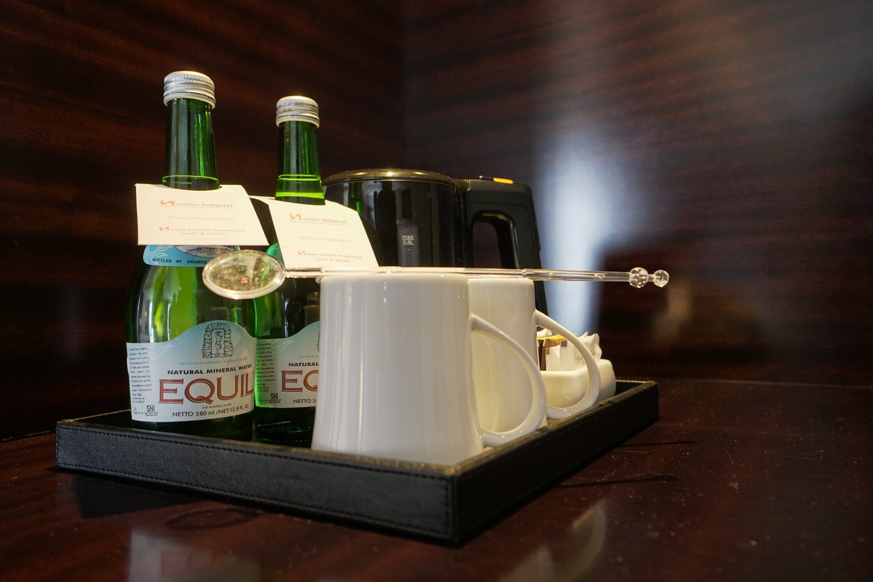 Una bandeja con dos botellas de EquiWater, una cafetera y un juego de tazas sobre una mesa de madera.