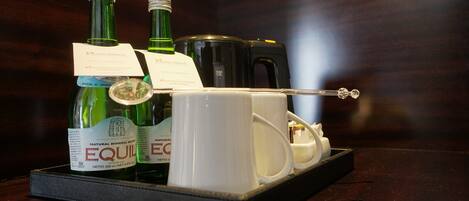 Una bandeja con dos botellas de EquiWater, una cafetera y un juego de tazas sobre una mesa de madera.