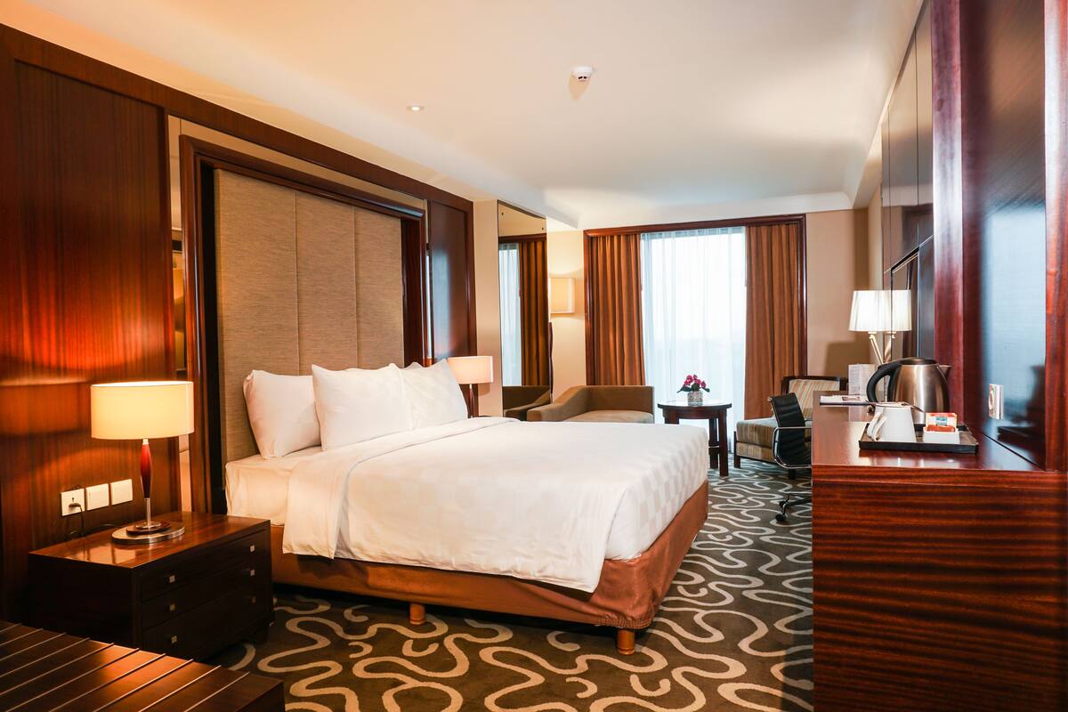 Une chambre d’hôtel avec un grand lit, un bureau avec une lampe, une chaise et une petite table avec une bouilloire.