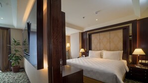 Une chambre d’hôtel avec un grand lit, un bureau, une chaise, une télévision, une lampe et une plante en pot.