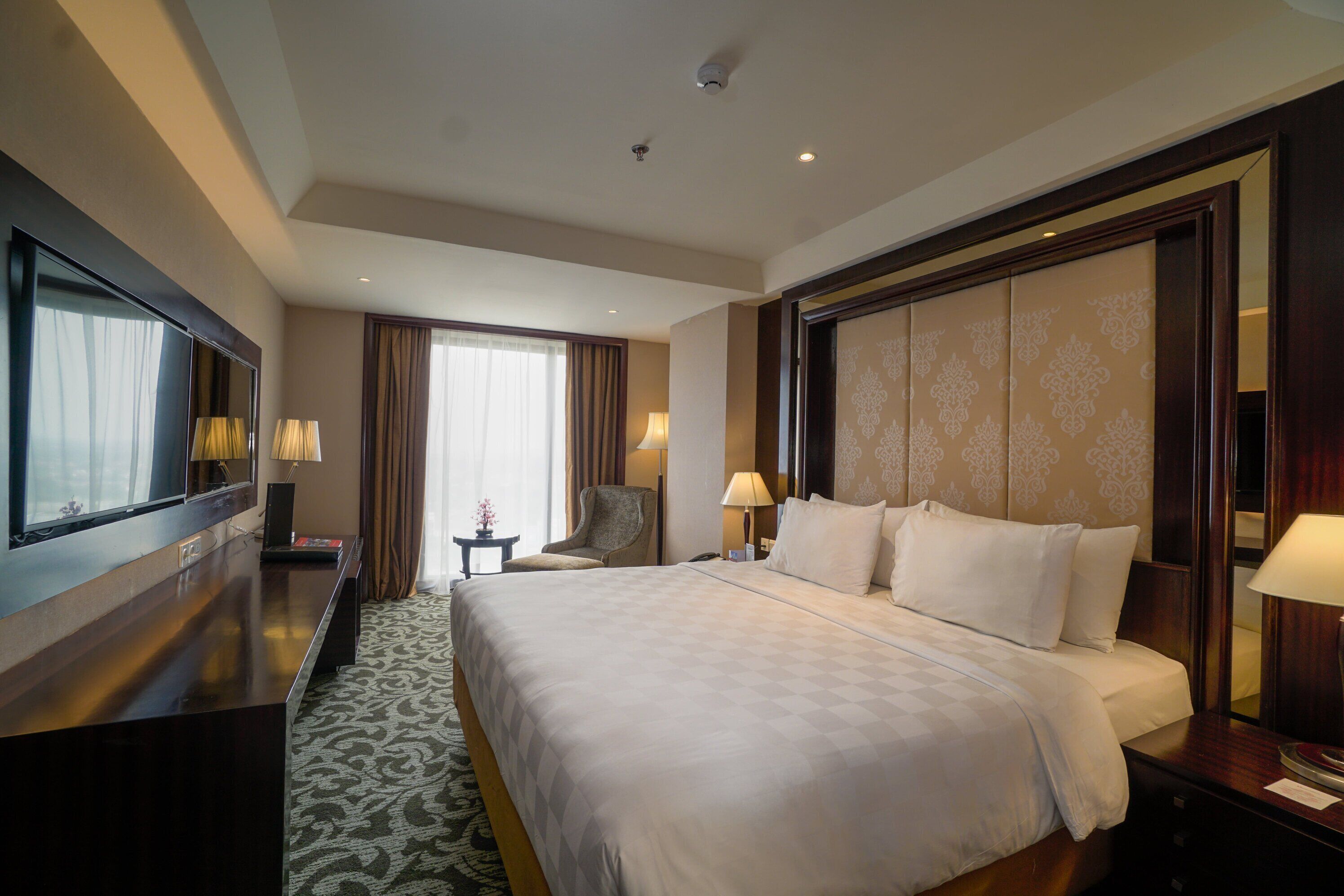 Quarto de hotel com uma cama grande, televisão, escrivaninha e uma cadeira.