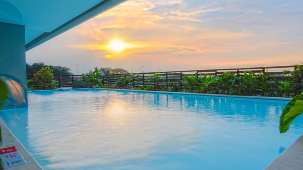 Une piscine avec vue sur le coucher de soleil, entourée de verdure et délimitée par une clôture en bois.