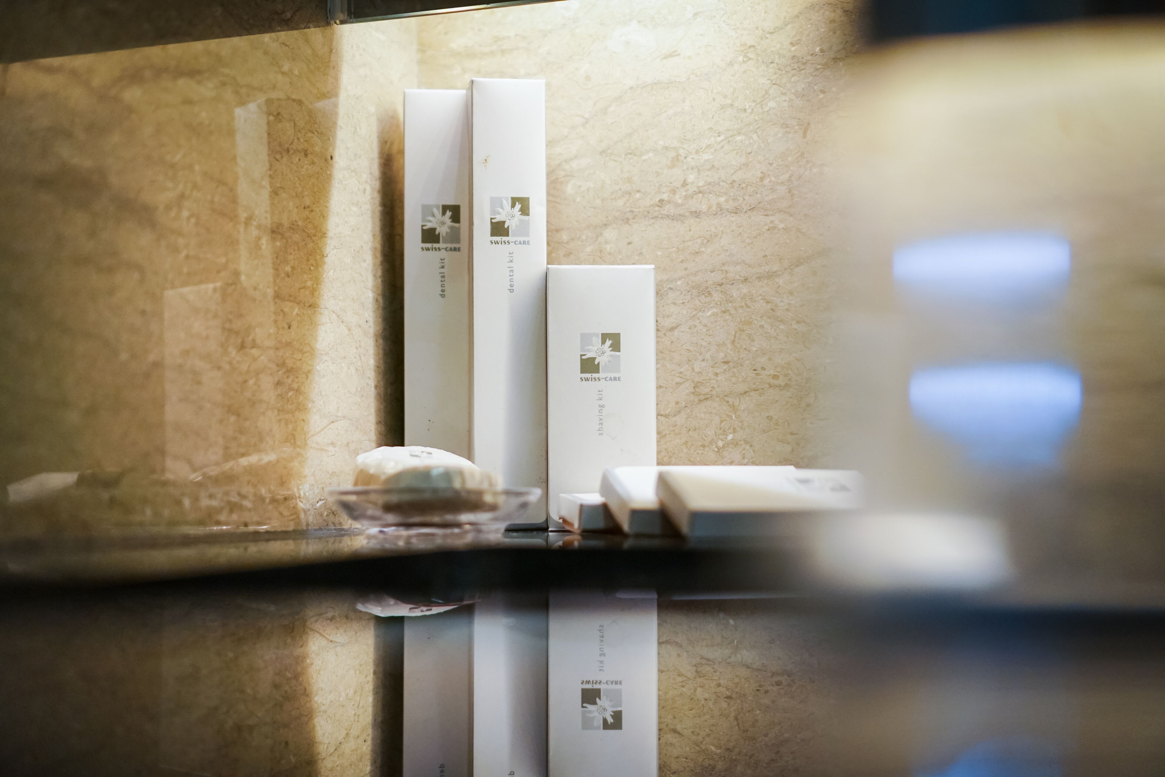 A bathroom with a marble countertop, a soap dish, and three white boxes labeled "SWISS-CARE."