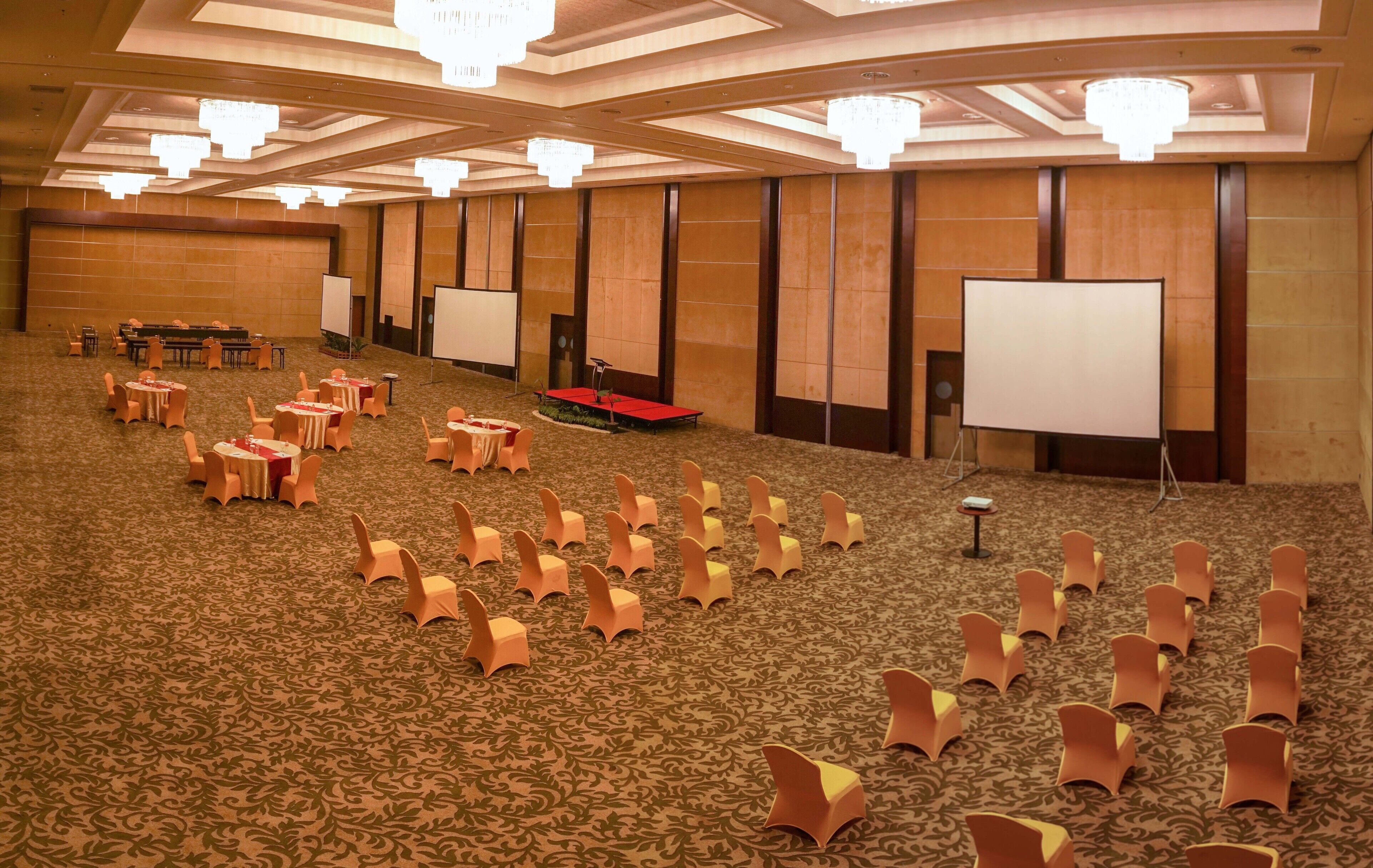 Un salón de conferencias con filas de sillas, un escenario con un atril y una pantalla grande.