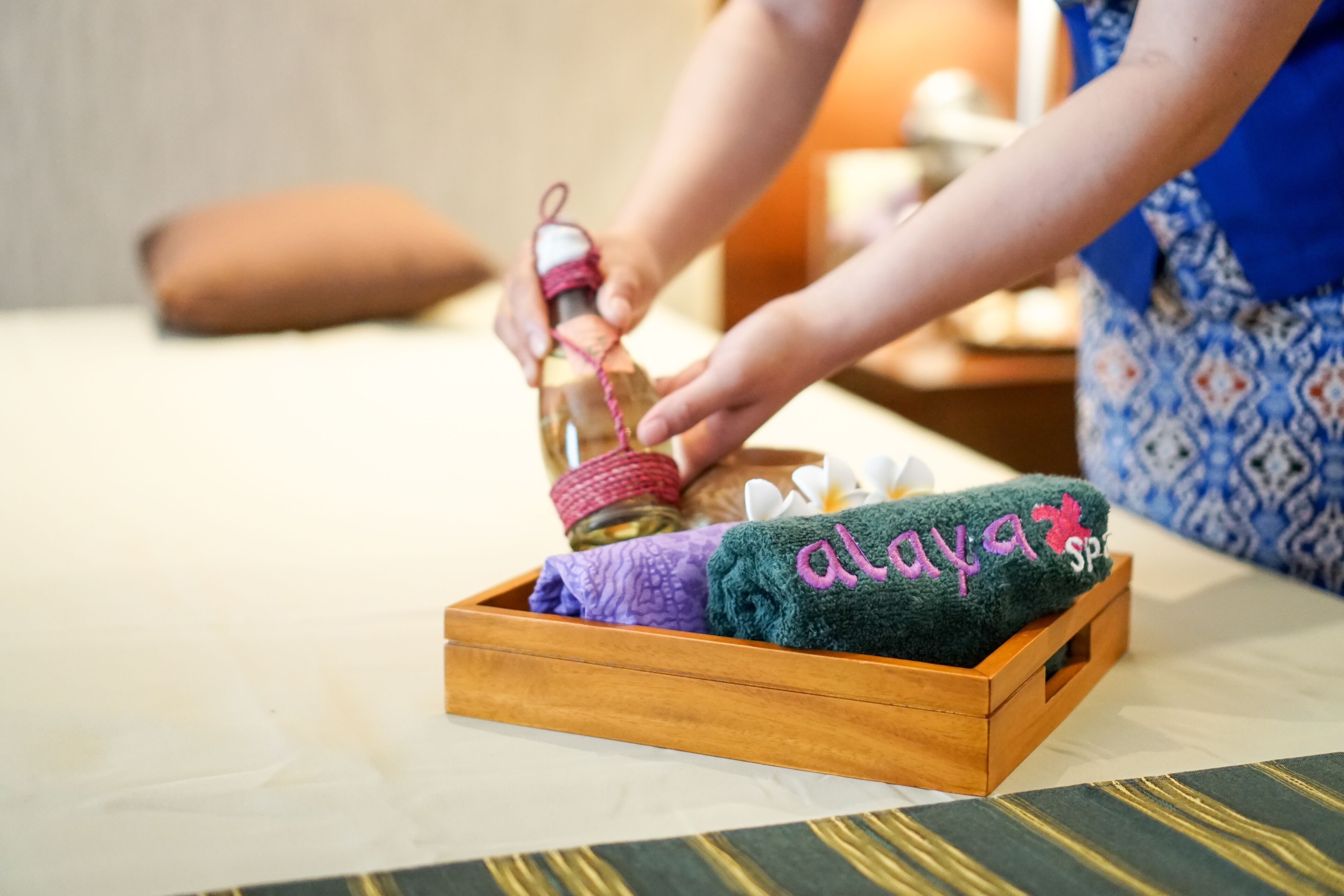 Un plateau en bois avec des serviettes et une bouteille, posé sur un lit.