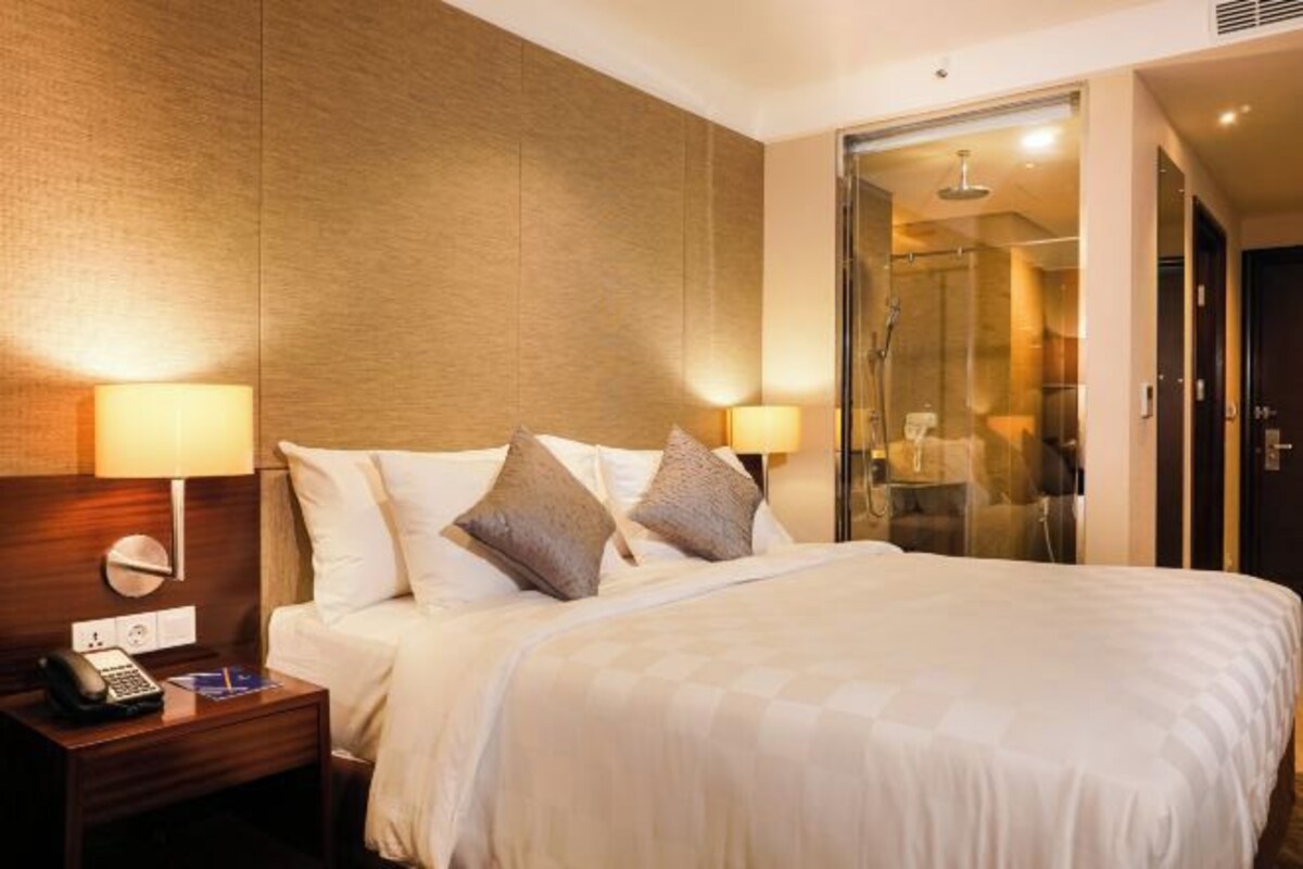 Une chambre d’hôtel avec un grand lit, deux lampes de chevet, une table de chevet avec un téléphone et une douche en verre.