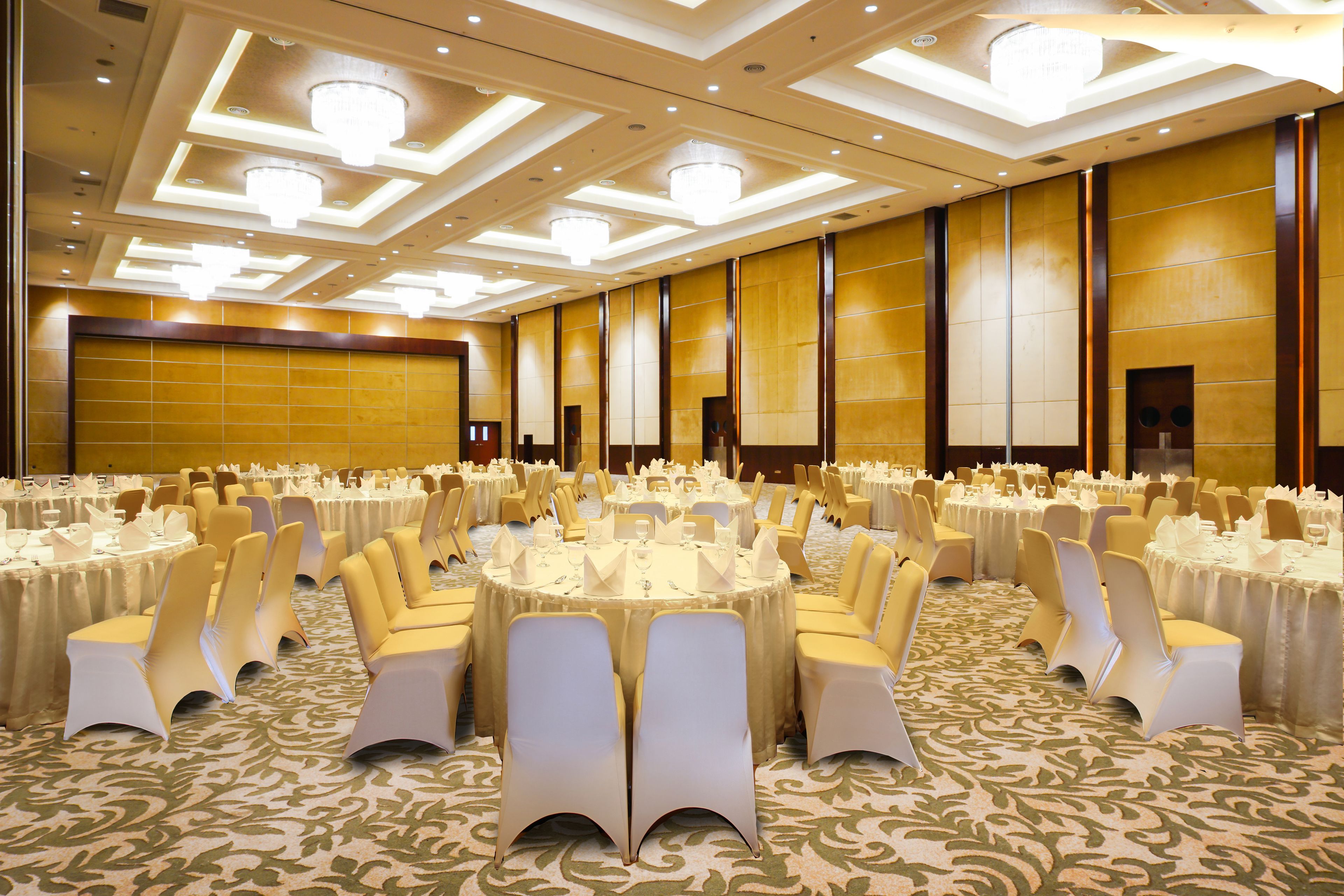 A banquet hall with round tables, white chairs, and chandeliers.