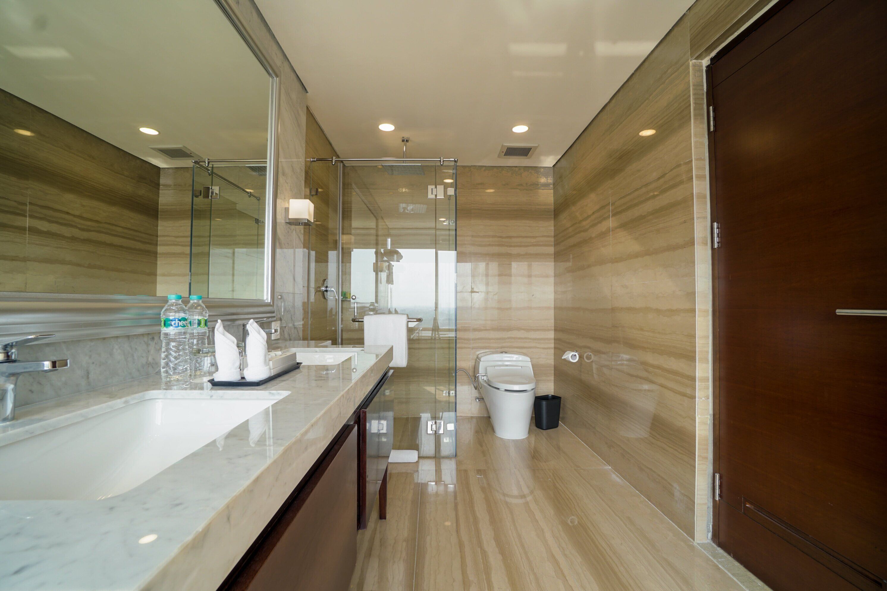 Un baño moderno con encimera de mármol, cabina de ducha de vidrio y puerta de madera.