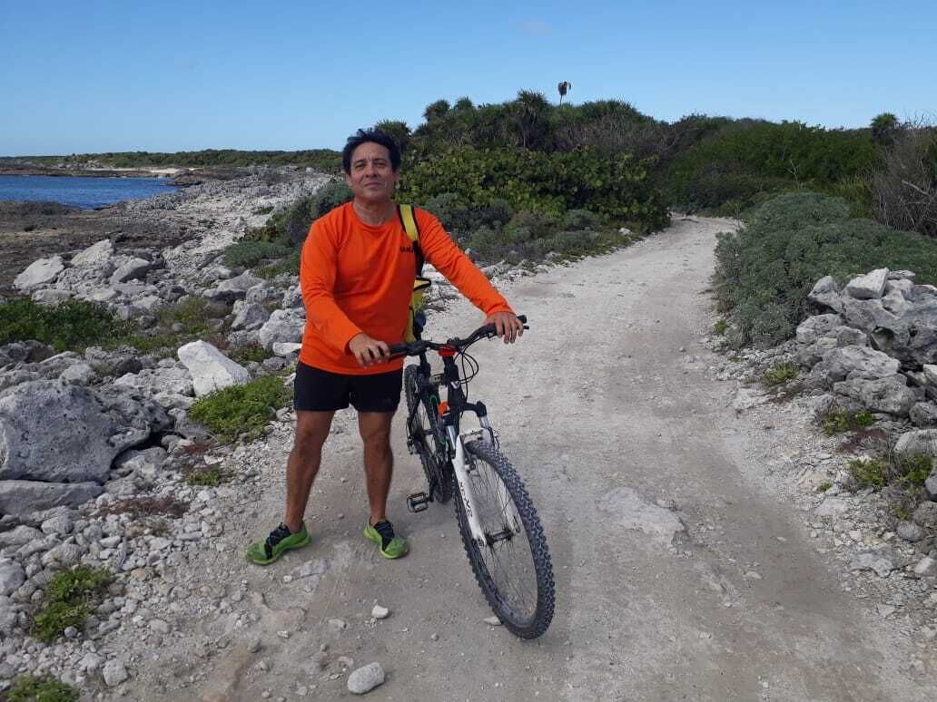 A person standing next to a mountain bike on a rocky path with a view of the sea and vegetation in the background.