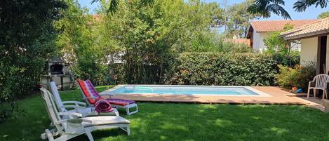 Un patio trasero con piscina, una parrilla y dos sillones de descanso.