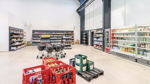 Uma loja ampla com corredores largos, prateleiras repletas de diversos produtos e uma exposição central de churrasqueiras.