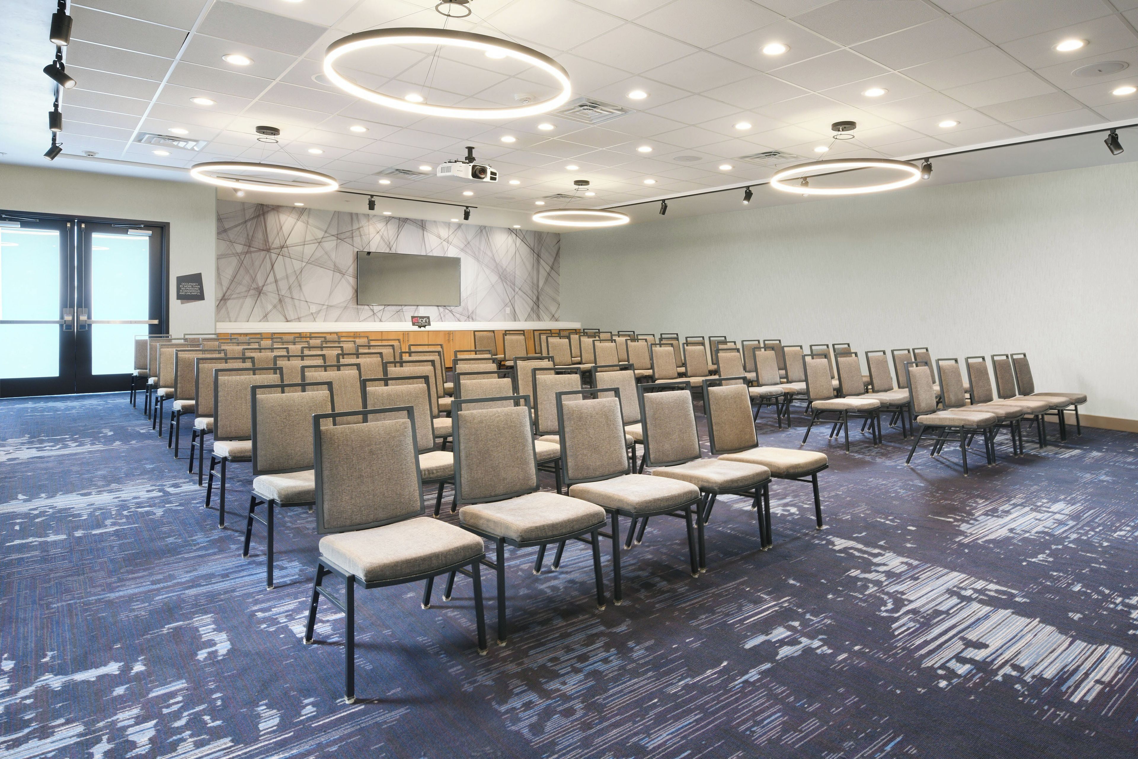 Un salón de conferencias con filas de sillas, un atril y una pantalla grande.