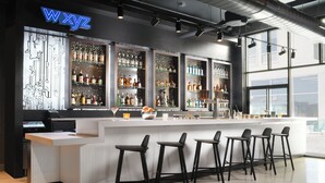 Una zona de bar con un mostrador blanco, taburetes negros y estanterías llenas de botellas de licores.