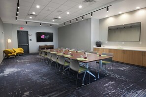 A conference room with a long table, chairs, a TV screen, and a kitchenette area. - Aloft by Marriott Dallas Euless (Euless)