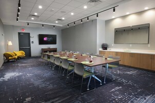A conference room with a long table, chairs, a TV screen, and a kitchenette area.