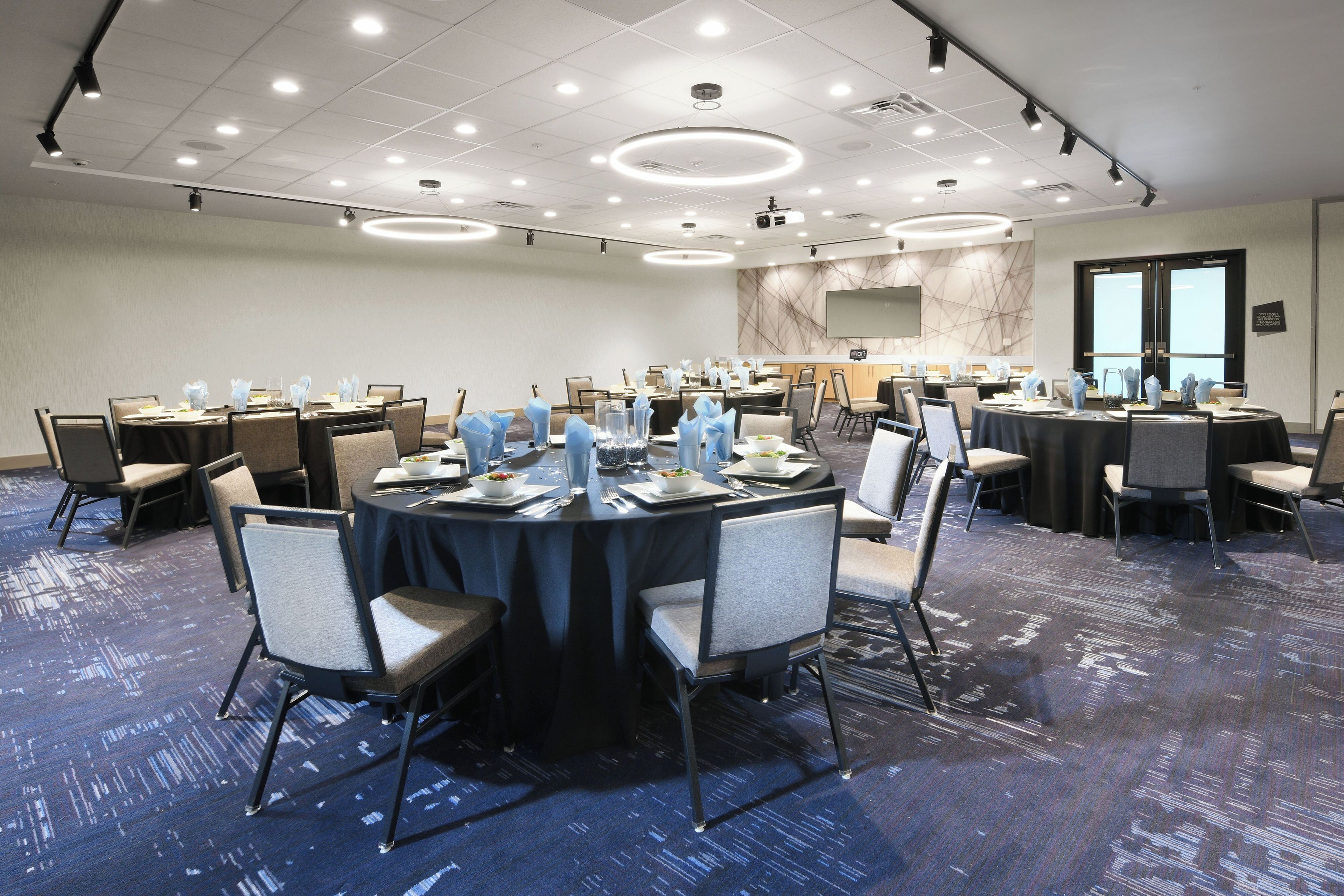 Une salle de conférence équipée de tables rondes, de chaises et d’un grand écran.