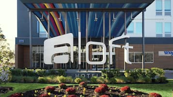 A hotel with a modern facade, a large sign with the name 'Eloft', and a well-maintained garden with red flowers.
